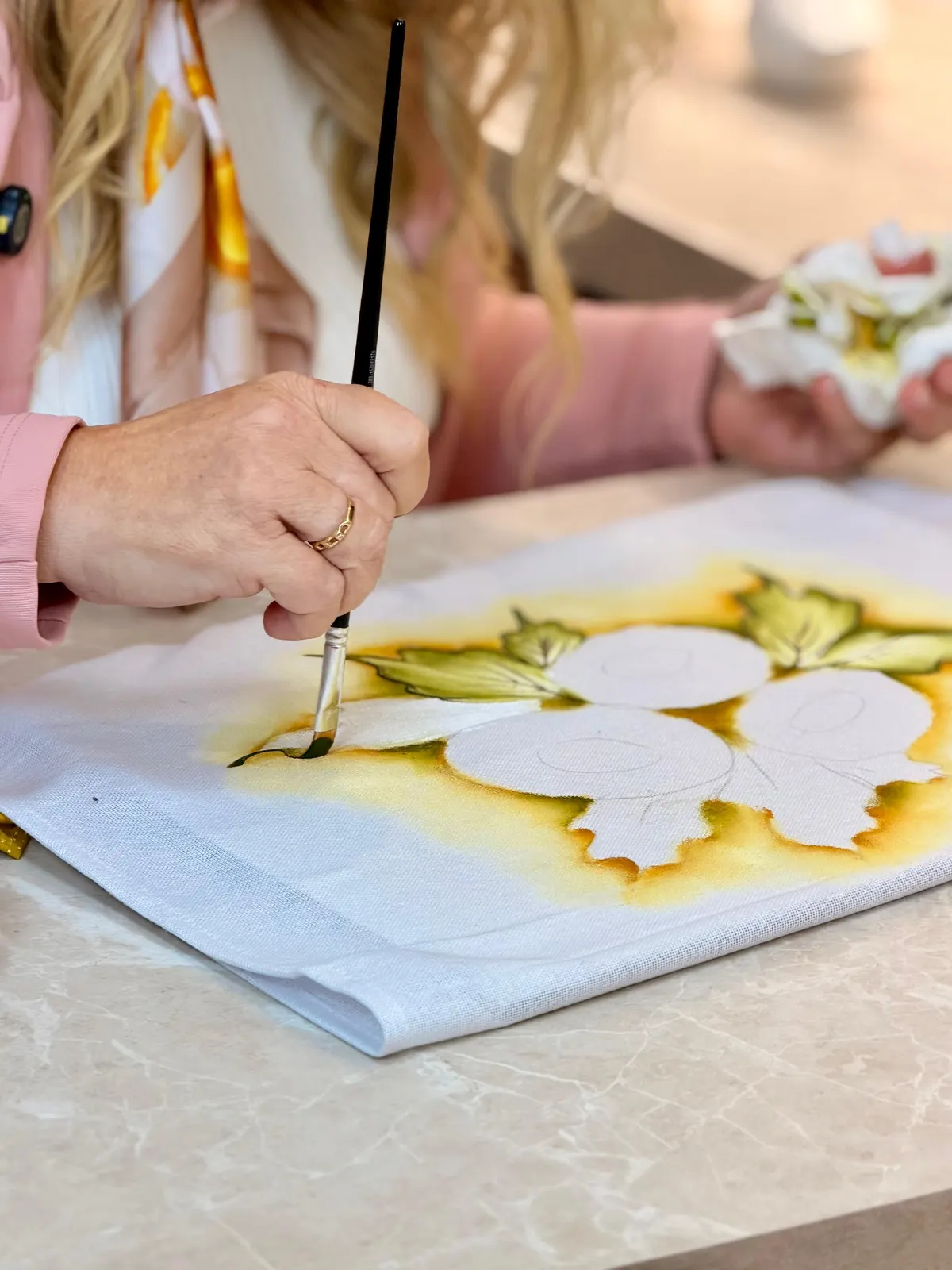 Close das mãos de Marisa pintando só o contorno branco, antes das cores